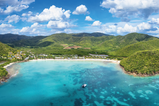 Blick vom Meer aus auf eine gr&uuml;n bewachsene Bucht in der Karibik